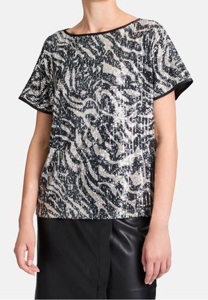 Vrouw draagt een top met korte mouwen bedekt met pailletten in een zwart-zilveren abstract zebrapatroon, gecombineerd met een zwarte leren rok.