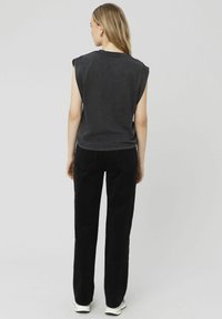 Haut noir sans manches avec des bords bruts, associé à un pantalon en velours côtelé noir taille haute. Le matériau semble doux, avec une coupe décontractée et des jambes droites.