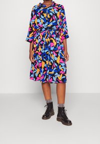 Färggklad skjortklänning med trekvartslånga ärmar, med ett blommönster i rosa, blått, orange och svart; midjebälte.