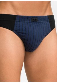 Slips da bagno a righe blu navy con vita nera, realizzati in morbido tessuto, con un'etichetta di marca sul lato anteriore sinistro.