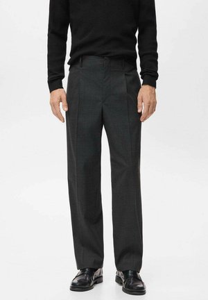 Pantalon gris avec une coupe ajustée, présentant un motif à carreaux subtil, une texture lisse et un pli sur le devant ; associé à des chaussures noires.