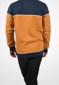 Sweat-shirt à manches longues avec corps orange, épaules bleu marine et bande d'accent blanche. Tissu doux avec poignets et ourlet côtelés.