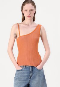 Oranje geribde tanktop met één brede schouderband, strakke pasvorm en gestoffeerde stof. Gecombineerd met hoge blauwe jeans.