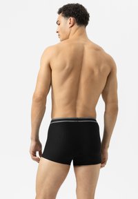 Boxers ajustés noir à côtes avec un design épuré ; la ceinture élastique présente deux bandes grises. Modèle vu de dos, teint de peau visible.