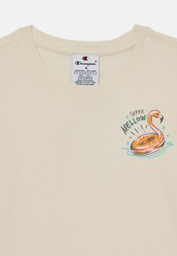 Kreminė medvilninė marškinė su spalvingu iliustracija apie flamingo plaukimo ratą ir užrašu "Super Mellow" priekyje. Apvalaus kaklo dizainas.