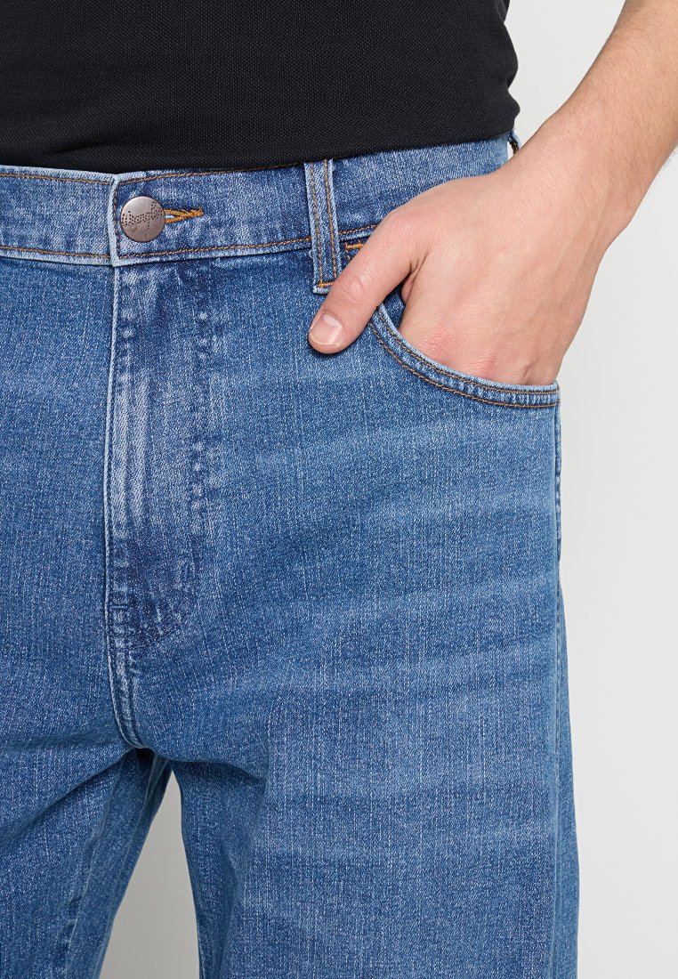 Jasnoniebieskie dżinsy o prostym kroju, z tradycyjnym pięci pockets designem i widocznym przeszyciem. Pasek w talii posiada metalowy guzik.