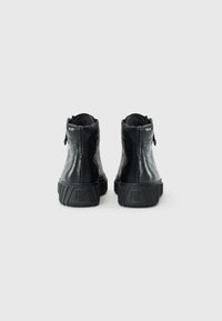Bottines en cuir noir avec des semelles en caoutchouc texturé, dotées d'une fermeture éclair à l'arrière et d'un design arrondi. Fini lisse et col rembourré.