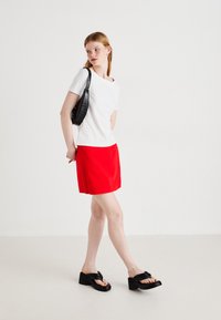 Bijela majica s kratkim rukavima, crvena suknja, crna torba preko ramena i crne platforme. Minimalistički dizajn s glatkom teksturom.