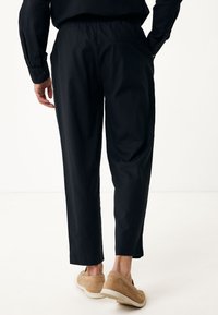 Svarta, avslappnade byxor med elastisk midja, med en slät yta och avsmalnande ben, i kombination med beige slip-on skor.