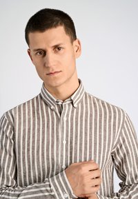 Camisa de botones a rayas en colores marrón y crema, con un cuello sólido, mangas largas y un tejido texturizado con líneas verticales.
