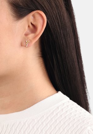 Orecchino a cuff in tono oro con un design intrecciato e un accento di pietra bianca. Indossato all'orecchio di un modello con capelli scuri e lisci e una maglietta bianca texturizzata.