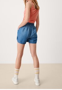 Denim shorts dengan pinggang elastis, warna biru, saku samping, dan hem dilipat. Dipasangkan dengan kaos tanpa lengan warna koral dan kaus kaki bergaris.