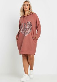 Huppari mekko pölyruusunvärisessä sävyssä, jossa on paljetein koristeltu sydänkuvio, pitkät hihat, sivutaskut ja rento istuvuus. Koristeltu nyöreillä.
