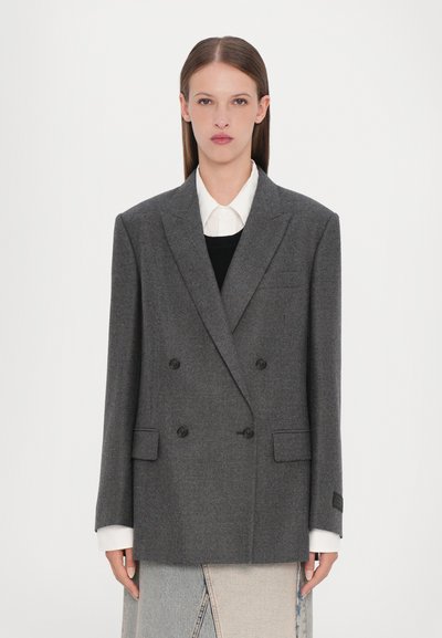Grijs dubbelgebreid blazer van textuurstof, met twee zakken en zwarte knopen. Draag het over een zwart topje en een wit shirt.
