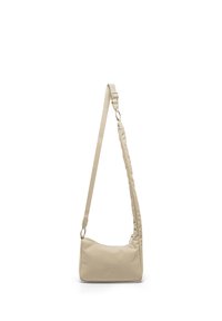 Beige olkalaukku, jossa säädettävä hihna ja pieni logo edessä, roikkuu valkoista taustaa vasten.