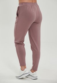 Ljusrosa atletiska joggers med elastisk midja, sidfickor, avsmalnande ben och slät textur, i kombination med vita sneakers.