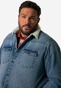 Camicia di denim con colletto in pelliccia sintetica di colore azzurro chiaro, due tasche sul petto e chiusura a bottoni. Presenta una tintura media e un design rilassato.