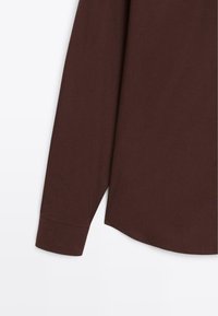 Brun langærmet skjorte med en glat tekstur, der har en afrundet kant og en standard knap-manchet detalje.