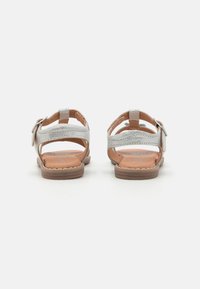 Silberne Leder-Sandalen mit einem Rückengurt und seitlicher Schnalle, mit einem strukturierten Muster, flacher brauner Sohle und offenem Design.