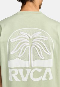 Hellgrünes T-Shirt mit einem strukturierten weißen Palmbaum-Design und fettem weißen "RVCA"-Text im unteren Bereich.