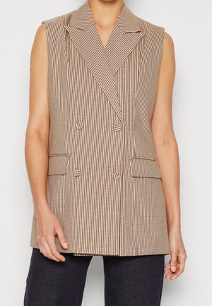 Bez rękawów dwurzędowa marynarka z brązowo-białym wzorem pepitki, z klapami z wycięciem, kieszeniami z patkami, noszona na ciemnych spodniach.