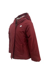 Giacca isolante rossa con cappuccio, chiusura con zip, due tasche laterali e logo sul petto. Tessuto liscio e leggermente lucido.