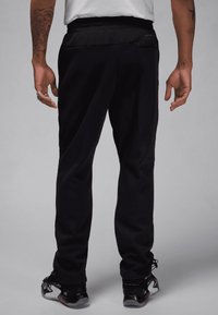Zwarte sportbroek met een tapered fit, elastische tailleband en zijzakken. De stof lijkt glad en elastisch, geoptimaliseerd voor comfort.
