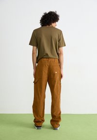 Pantaloni din cută maro, cu multiple buzunare, asortați cu un tricou verde măsliniu. Stilul este lejer, cu un design pe picior drept.