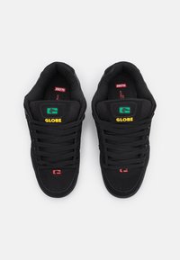 Černé tenisky s texturovaným povrchem, s žlutým a zeleným logem "GLOBE", černými tkaničkami a červenými akcenty na stélkách.
