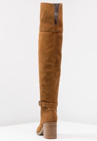 Hnědé semišové kozačky nad kolena s vysokým blokovým podpatkem, nastavitelného přezkou a výřezem v horní části pro zvýšení stylu.