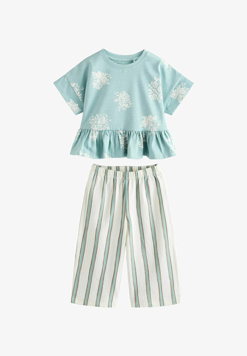Jasnoniebieska bawełniana koszulka z białymi, kwiatowymi wzorami i falbaną na dole, w połączeniu z białymi i zielonymi pasiastymi spodniami o szerokich nogawkach oraz elastycznym pasem.