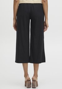 Černé široké kalhoty culottes z lehké látky, které mají volný střih. Spodní okraj je rovně střižený, doplněný o sandály s průhledným blokovým podpatkem.