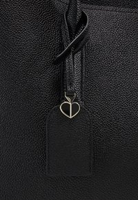 Borsa in pelle nera dalla texture lavorata, con un ciondolo a forma di cuore e un’etichetta. Il design comprende una tracolla liscia per il trasporto.