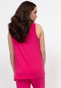 Fuchsia mouwloos topje met een zachte textuur en een ontspannen pasvorm, voorzien van een ronde zoom en zijsplitten voor extra comfort.