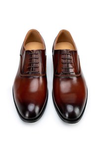 Zapatos de vestir de cuero marrón con cordones, de textura suave, puntera redondeada y costuras en contraste, con un acabado pulido y diseño minimalista.