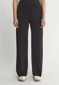 Czarne spodnie szerokie z miękkiego materiału, z gładkim elastycznym paskiem w talii i luźnym krojem, w połączeniu z białymi trampkami.