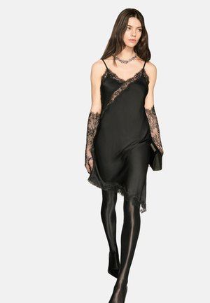 Robe en satin noir avec bordure en dentelle, présentant un design diagonal et des bretelles fines. Associée à des gants en dentelle et des collants noirs. Silhouette simple et élégante.