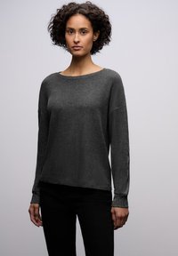 Tummanharmaa pitkähihaine neule, jossa on leveä pääntie, rento istuvuus ja teksturoitu kangas; hihansuissa hienovarainen kimallus.