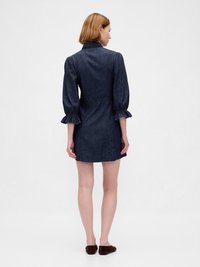 Abito in denim con vita aderente, maniche a sbuffo e polsini arruffati. Di un blu scuro, con cuciture minime, lunghezza fino a metà coscia.