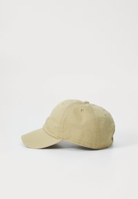 Khaki baseball cap with a curved brim, made of textured fabric. Features ventilating eyelets and an adjustable strap at the back.