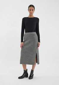 Jupe tricotée grise avec une fente sur le côté, taille côtelée, associée à un haut noir à manches longues et des bottines noires. Design simple et texturé.