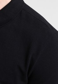 Polo shirt en coton noir, avec un col classique, un tissu texturé et des manches courtes, offrant une finition lisse et des détails de couture subtils.