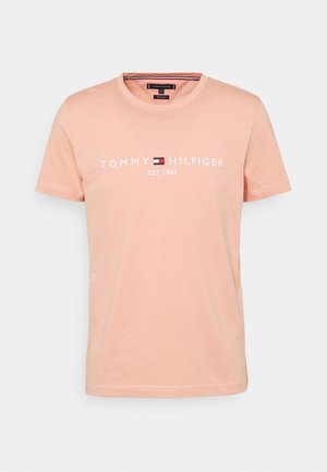 T-shirt corta in cotone color pesca chiaro con maniche corte e scollo tondo, con testo "Tommy Hilfiger EST. 1985" e logo nei colori bianco, rosso, blu navy e bianco.