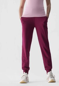 Burgunderrote Sweatpants mit elastischen Bündchen und Seitentaschen, kombiniert mit einem hellrosa Oberteil und weißen Sneakers mit mehrfarbigen Akzenten.