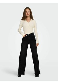Langærmet, ribbet cremetop med V-udskæring og tre knapper, parret med højtaljede, vide sorte jeans. Glat stoftekstur.