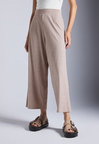 Světlé béžové široké kalhoty s vertikálním žebrovaným vzorem, doplněné hnědými sandály na platformě s robustní podešví a detailem přezky.