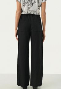 Pantalons larges noirs en tissu texturé, comportant deux poches arrière et une taille élastique pour un ajustement facile.