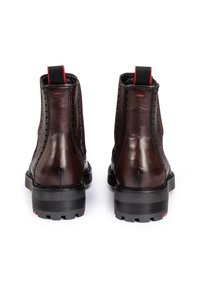 Brown leather ankle boots with black rubber soles, textured finish, red accents on pull tab and sole, and prominent stitched detailing.