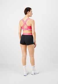 Różowy stanik sportowy z krzyżującymi się ramiączkami i białym napisem "NIKE PRO". Połączony z czarnymi szortami z podobnym wzorem pasa.