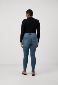 High-waisted, form-fitting blue jeans with a faded wash and two back pockets, paired with a black long-sleeve top and black sandals.